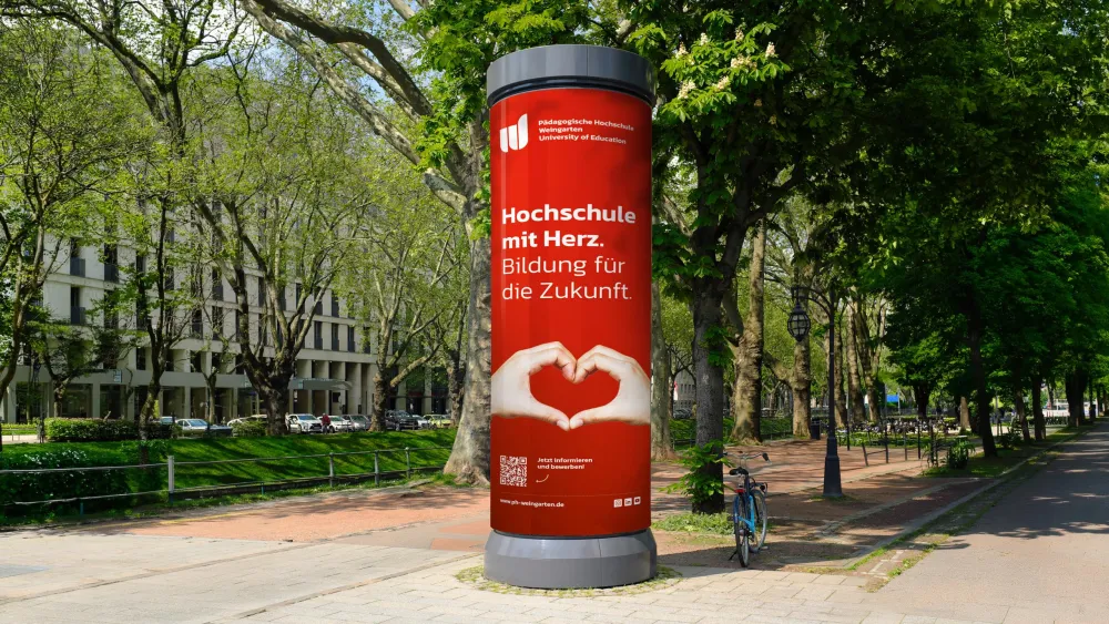 Rote Litfasssäule mit Herzsymbol in einem sonnigen Park