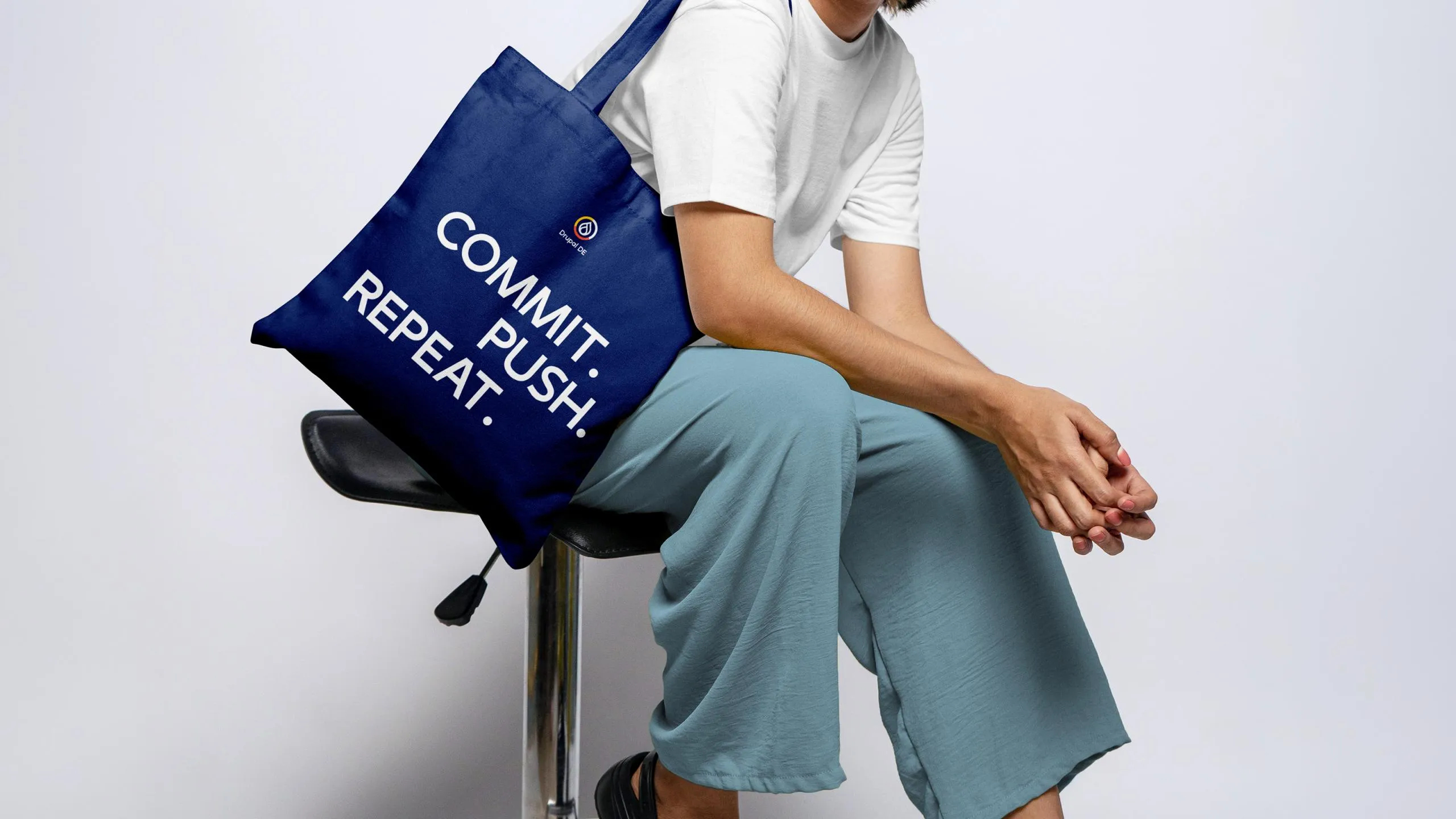 Person sitzt auf Stuhl mit blauer Stofftasche mit weißem Text